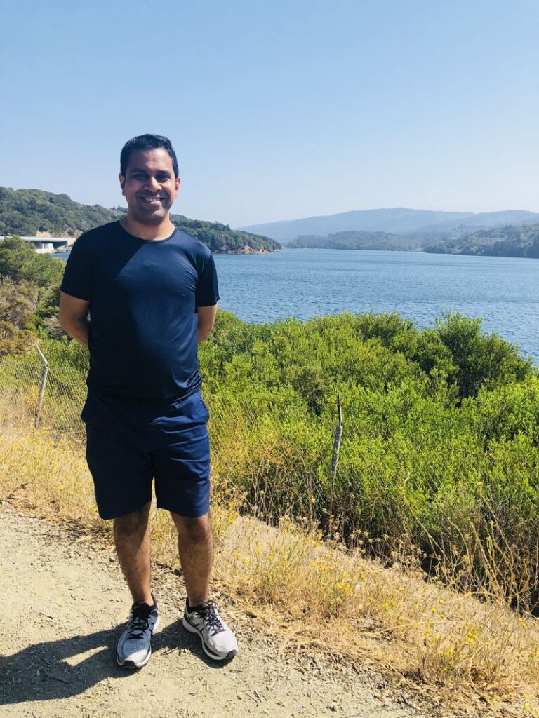 Man smiling by scenic lake on sunny day.