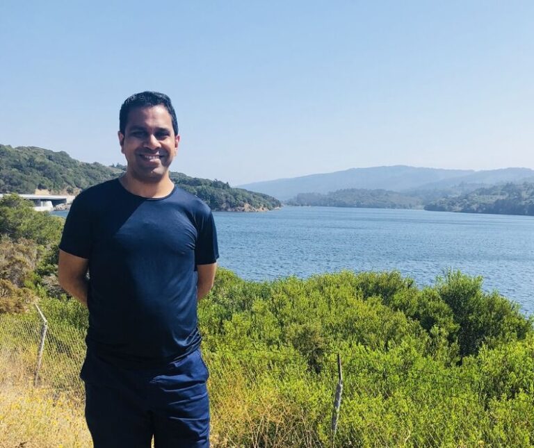 Man smiling by scenic lake and greenery.