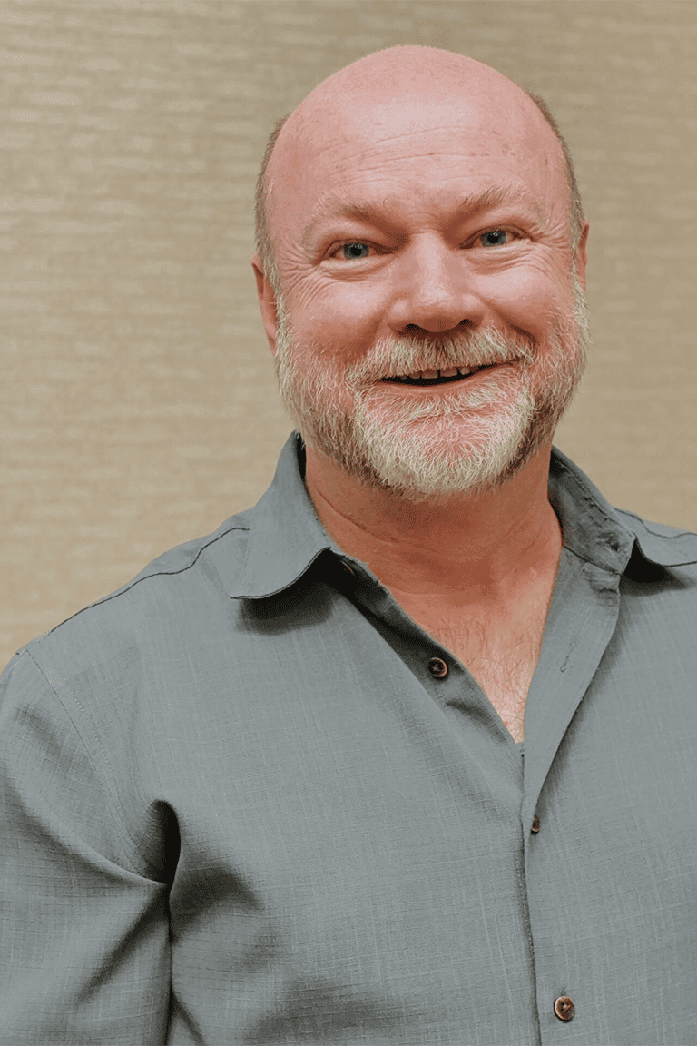 Smiling bald man in gray shirt indoors.