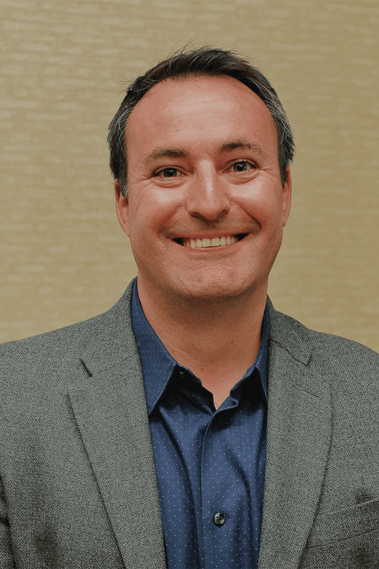 Smiling businessman in navy suit and polka-dot shirt.
