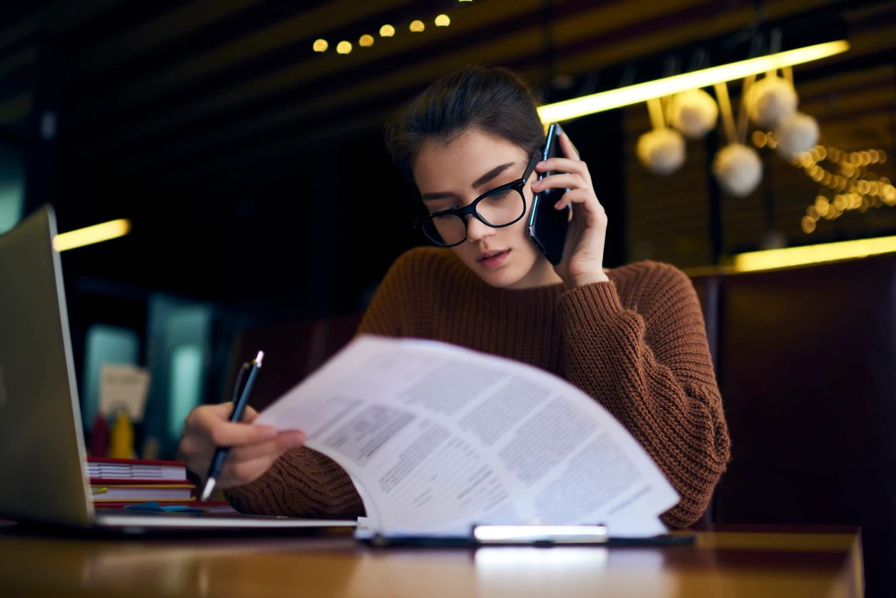 Woman multitasking with phone and documents at desk