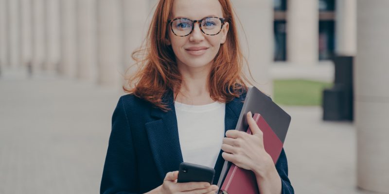 confident-beautiful-red-haired-female-business-consultant-holding-modern-smartphone-and-laptop.jpg